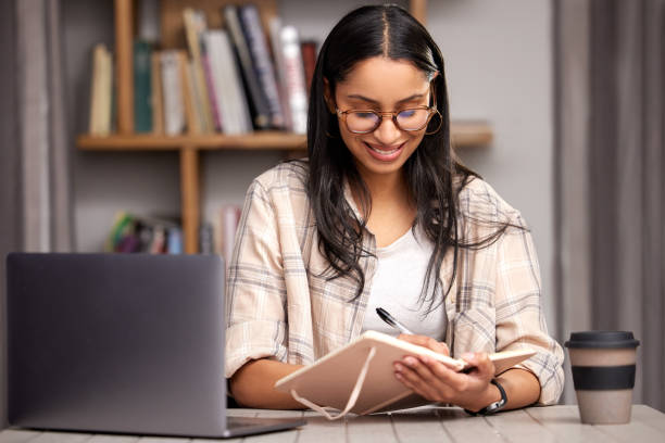 istock Cropped shot of an attractive young female student taking notes while studying in the library using her laptop 1369503490