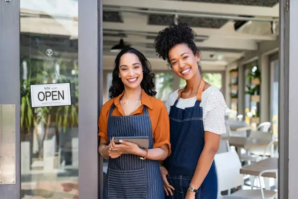 Photo of Two successful woman waitress standing at cafe entrance door