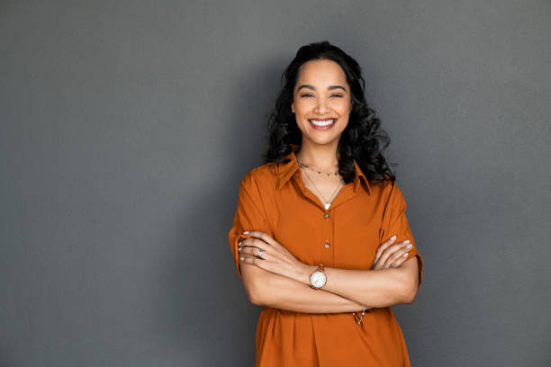 Beautiful successful latin woman smiling Portrait of a young latin woman with pleasant smile and crossed arms isolated on grey wall with copy space. Cheerful hispanic woman on grey background with copy space. Beautiful girl with folded arms looking at camera against grey wall. teeth photos stock pictures, royalty-free photos & images