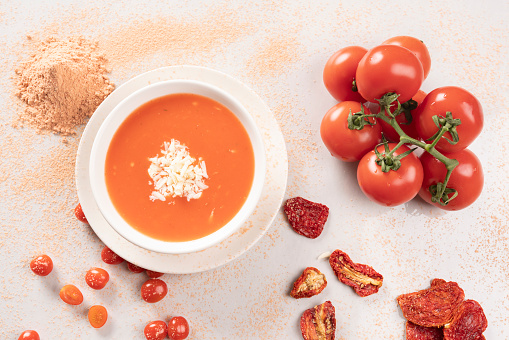 There are tomatoes, cherry tomatoes and sun dried tomatoes around the soup bowl.