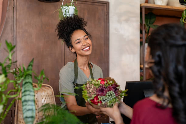 felice fiorista nero che vende fiori alla giovane donna - boutique owner store retail occupation foto e immagini stock