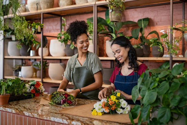 dwie wieloetniczne kobiety pracujące razem w kwiaciarni - kwiaciarnia zdjęcia i obrazy z banku zdjęć