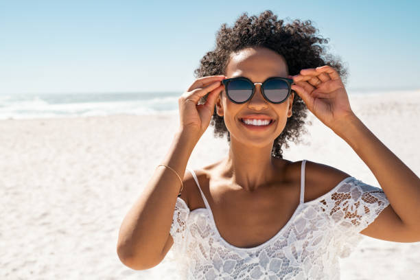 istock Smiling black woman having fun at beach while wearing sunglasses 1369509280