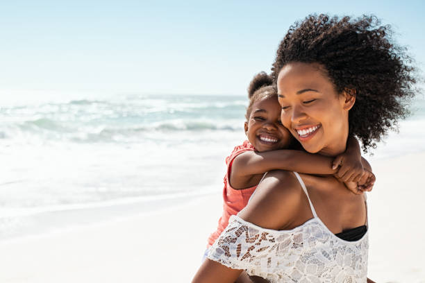 Happy mother giving daughter piggyback ride at beach Smiling young black mother and beautiful daughter having fun on the beach with copy space. Portrait of happy sister giving a piggyback ride to cute little girl at seaside. Lovely female kid embracing her lovely mom during summer vacation. beach holiday stock pictures, royalty-free photos & images