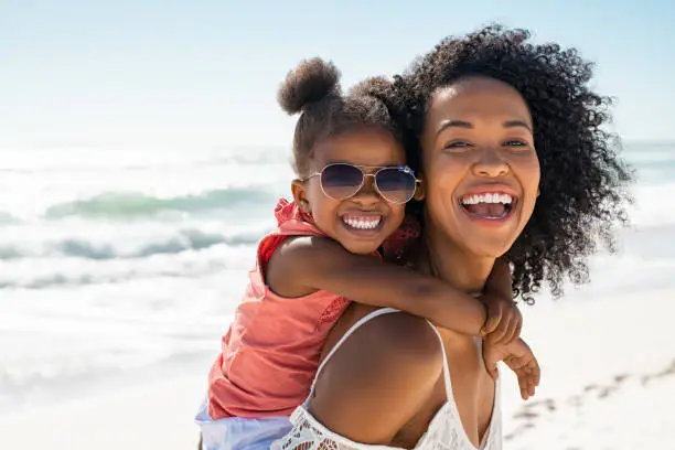 Photo of Happy young mother giving laughing daughter piggyback ride at beach