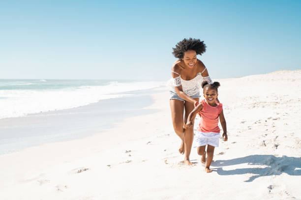 madre africana che corre dietro alla figlia sulla spiaggia - beach women joy sand foto e immagini stock