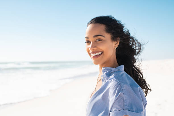 Portrait of natural beauty woman at beach Portrait of young woman at sea looking at camera. Smiling latin hispanic girl standing at the beach with copy space and looking at camera. Happy mixed race girl in casual outfit with wind in her hair. blowing photos stock pictures, royalty-free photos & images