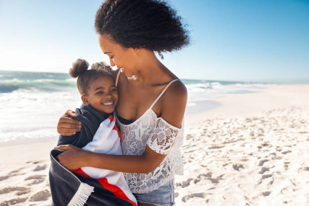 Lovely black woman hugging child with towel at beach
