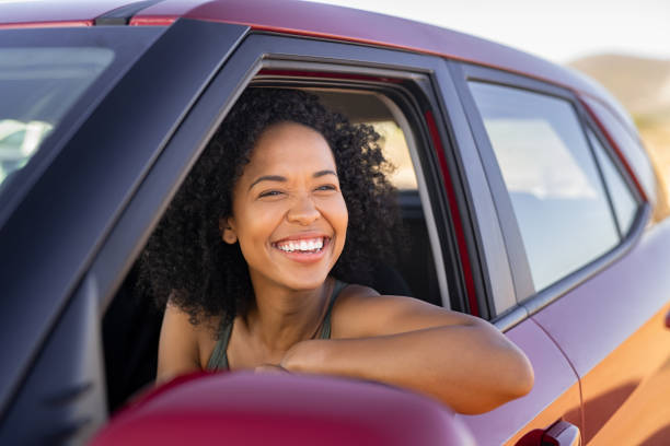 Black young woman looking outside car Beautiful african american woman looking outside car during summer holiday. Young attractive black woman laughing and enjoying road trip on a summer day. Happy girl driving a red car with big grin. driving stock pictures, royalty-free photos & images
