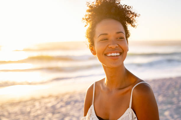 jeune femme africaine se relaxant à la plage au coucher du soleil - young adult beach people cheerful photos et images de collection