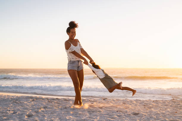 mulher girando em círculo sua filha na praia - swinging sister family child - fotografias e filmes do acervo