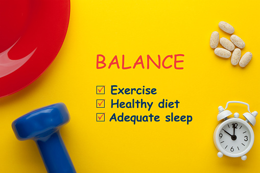 Balance between diet, exercise, and sleep concept with dumbbells, clock, vitamins end plate.