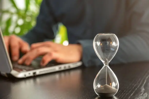 Photo of Hourglass with time running out in an office as a symbol of time pressure at work