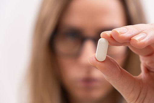 Close up of female hand holding white pill or capsule vitamin supplement close up.