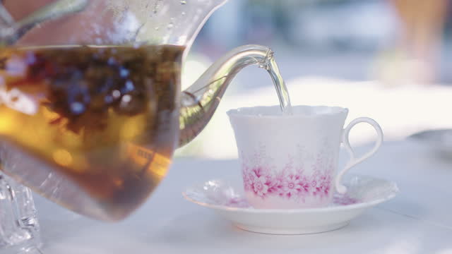 Pouring flower tea onto ornate tea cup in sunny day