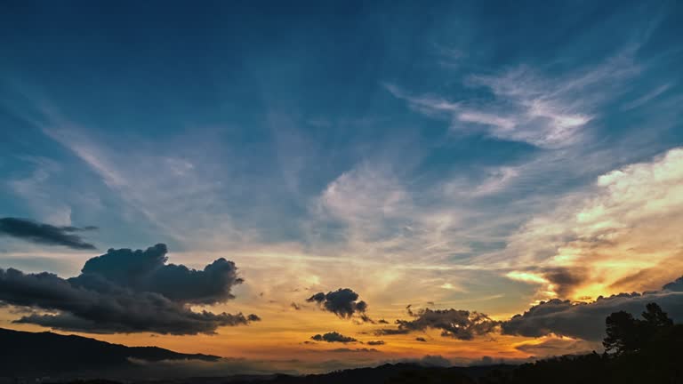Zeitraffer einer Tag-zu-Nacht-Sequenz mit Wolken, die sich schnell bewegen, und Sonnenstrahlen, die auf die hohen Wolken leuchten. Die Lichter der Stadt drehen sich langsam beim Betreten der Nacht.