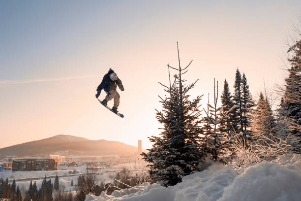 snowboarder che fa un salto in aria alto con afferrare il cielo soleggiato blu chiaro durante il tramonto sopra abeti e montagne - sheregesh foto e immagini stock