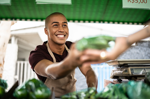 Vendedor entregando una verdura a un cliente en un mercado callejero photo