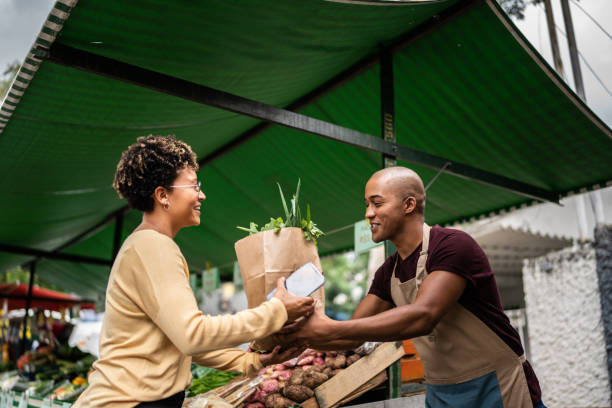 Seller handing the shopping bag to a customer at a street market Seller handing the shopping bag to a customer at a street market agricultural fair stock pictures, royalty-free photos & images