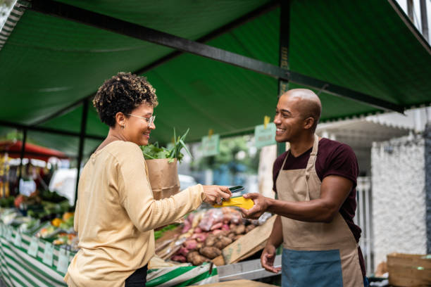 거리 시장에서 휴대 전화로 지불하는 젊은 여성 - market market stall shopping people 뉴스 사진 이미지