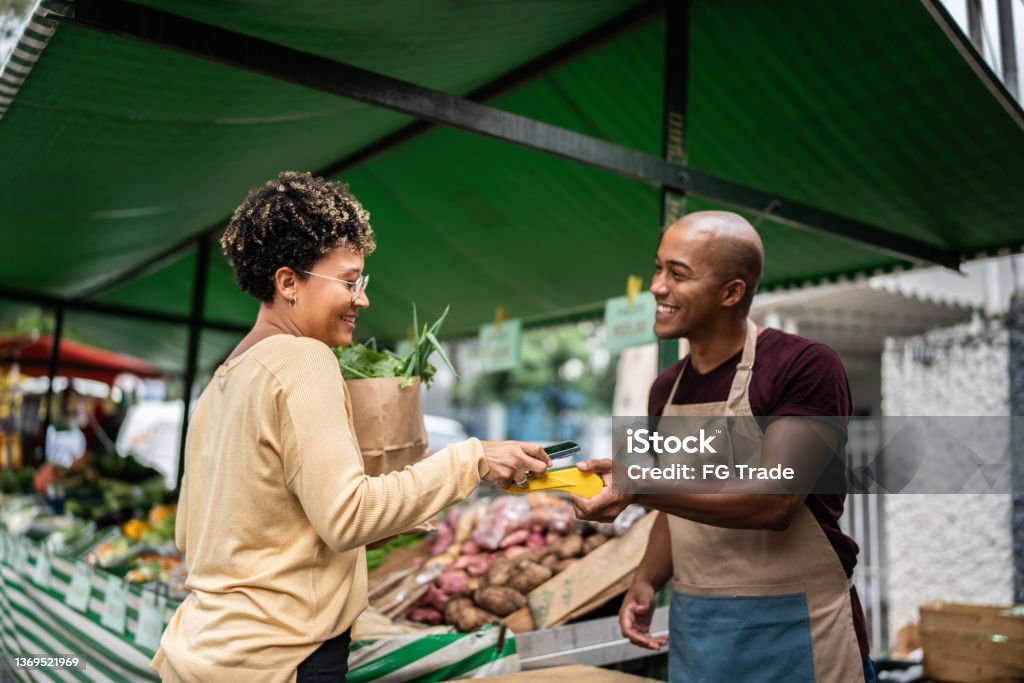 Young woman paying with mobile phone at a street market Agricultural Fair Stock Photo