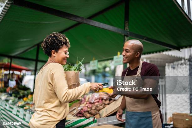 Young Woman Paying With Mobile Phone At A Street Market Stock Photo - Download Image Now