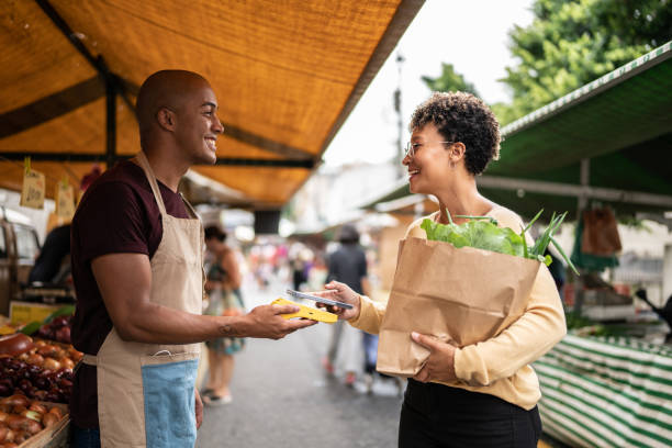 giovane donna che paga con il cellulare in un mercato di strada - farmers market foto e immagini stock