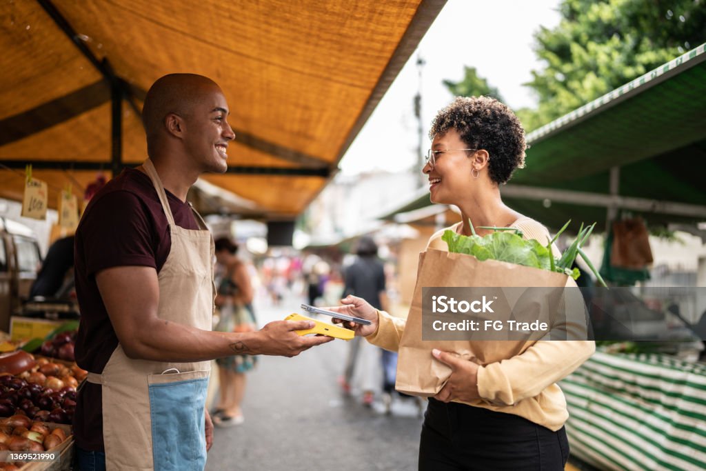 Young woman paying with mobile phone at a street market Paying Stock Photo