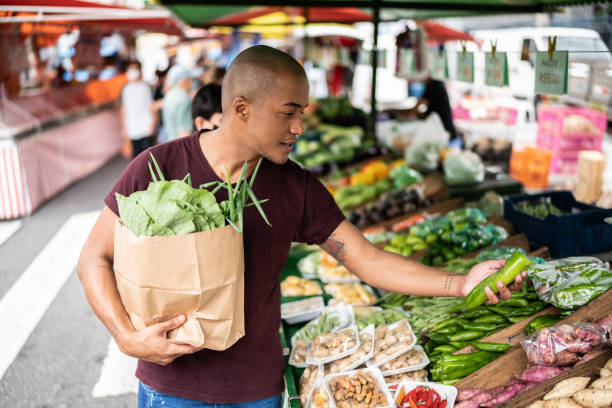 giovane che sceglie il cetriolo in un mercato di strada - farmers market foto e immagini stock