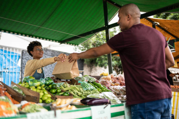 쇼핑백을 길거리 시장에서 고객에게 건네주는 판매자 - market market stall shopping people 뉴스 사진 이미지