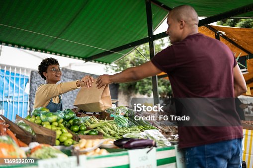 istock Seller handing the shopping bag to a customer at a street market 1369522070