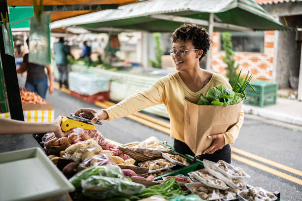 giovane donna che paga con il cellulare in un mercato di strada - supermarket groceries shopping healthy lifestyle foto e immagini stock