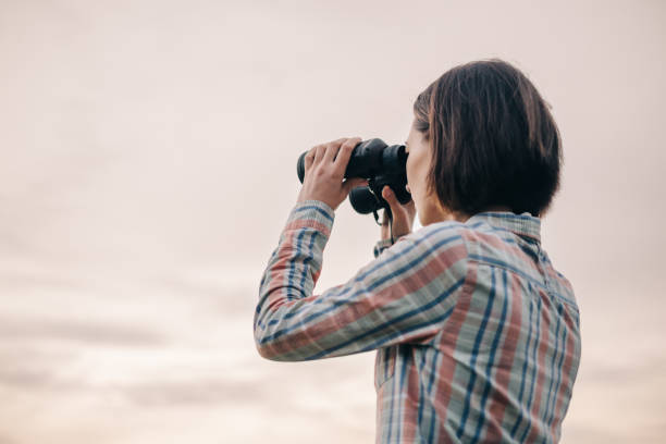 istock Woman looking through binoculars on background of sky. 1369522352