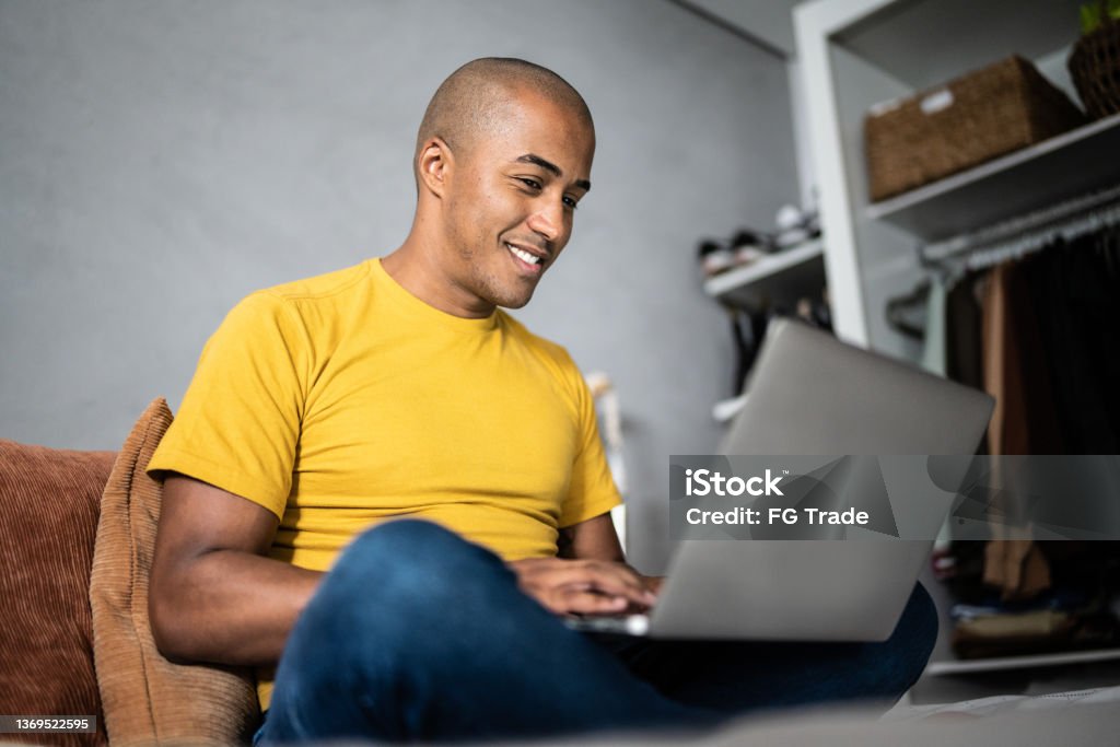Young man using the laptop in the bed at home Using Laptop Stock Photo
