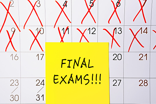 The phrase Final Exams written on a yellow sticky note posted on a calendar or planner page as a reminder. Closeup of a personal agenda