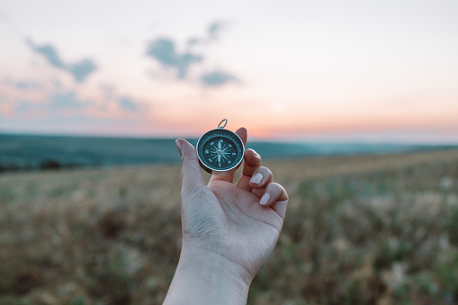 Compass, nautical compass, travel compass in tourist hand on wheat field background at sunset