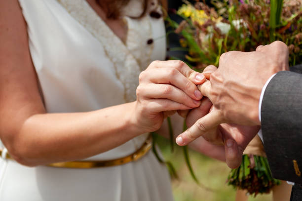 istock Young bride put wedding ring on the groom's finger with difficulties, close-up. Wedding ceremony, hardly exchanging. Future husband wearing a wedding ring. Swollen finger. 1369525387