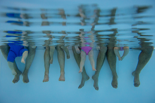 An unrecognisable group of people and their baby's legs in a swimming pool in Boldon, North East England during a baby swimming class.