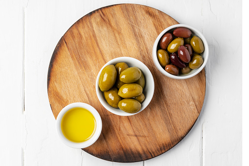 Small bowl with olive oil and olives on white background, top view, flat lay