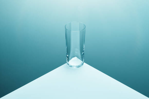 Emtpy clear drinking glass at the edge of a white table with soft gradient at background