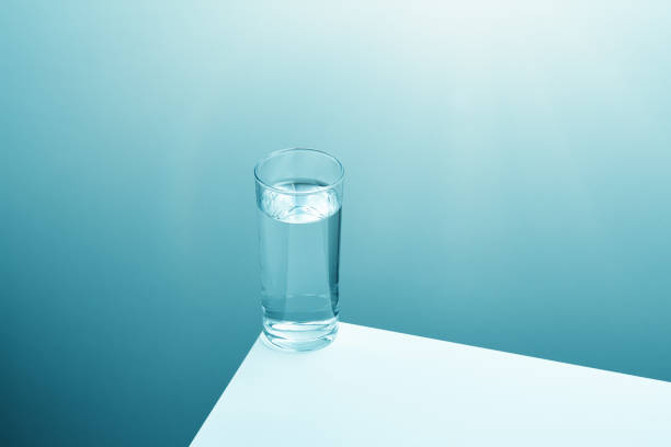 klares glas trinkwasser am rand eines weißen tisches mit weichem gefälle im hintergrund - glass rim stock-fotos und bilder