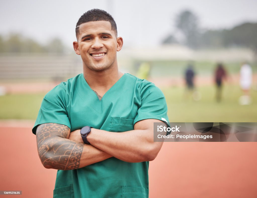 Cropped portrait of a handsome young male paramedic standing with his arms folded on a track outside Let's get you patched up Tattoo Stock Photo