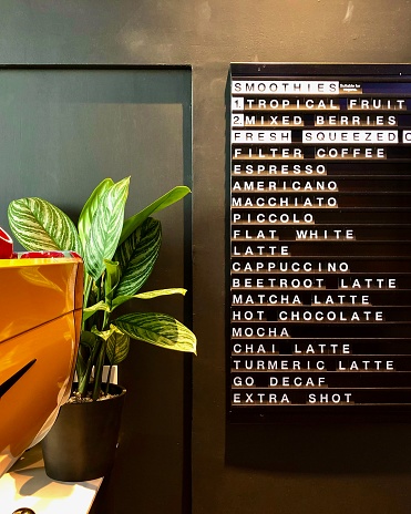 Drinks menu board in central London cafe, with a plant and yellow espresso machine
