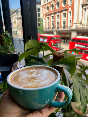An oat milk latte decorated with a swan overlooks red buses and shops on London's Oxford Street