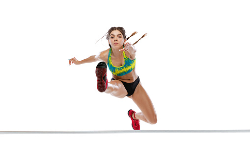 Sport of racing over hurdles. One sportive, muscular girl jumping, running isolated on white background. Overcoming, competition, achievements concept. Concept of action, motion, youth, health.