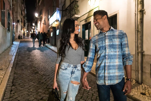 Happy multiracial couple smiling and walking at night in Lisbon stock photo