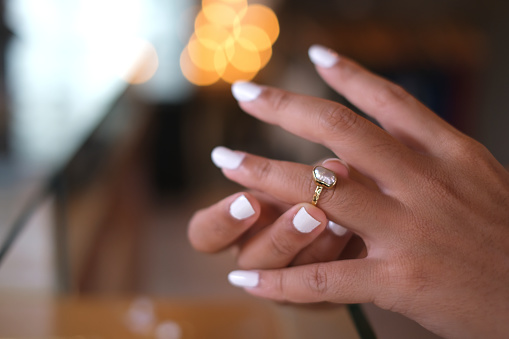 Close-up shot of an unrecognizable Asian woman with a white manicure inserting a ring into her ring finger at a jewelry store.