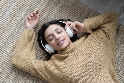 Portrait of a relaxed woman listening to music with headphones lying on a carpet at home