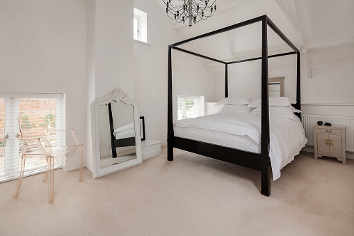 Luxury modern furnished chic bedroom in white with dark wood four poster bed and prominent mirror with ornate white painted frame
