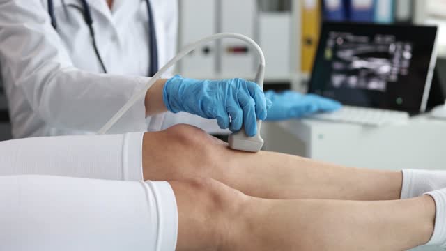 Doctor in rubber gloves scans patient leg with ultrasound machine